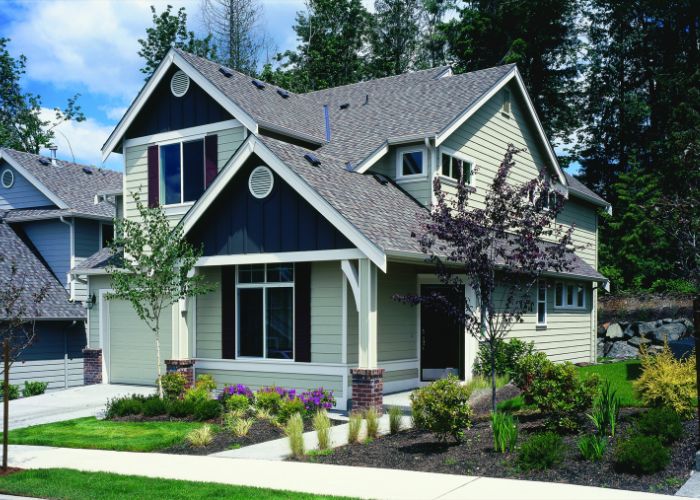 Two-story home with gray and dark blue siding, gabled roof, and a landscaped yard featuring shrubs, flowers, and small trees in Loveland